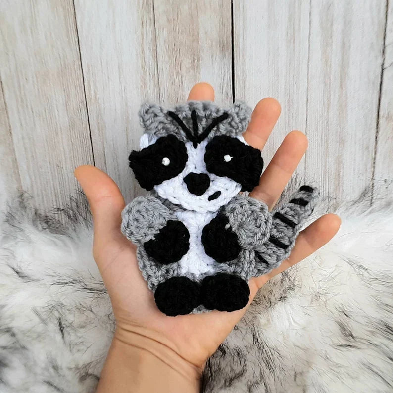 Finished crochet raccoon applique with gray body, black eye patches, and striped tail