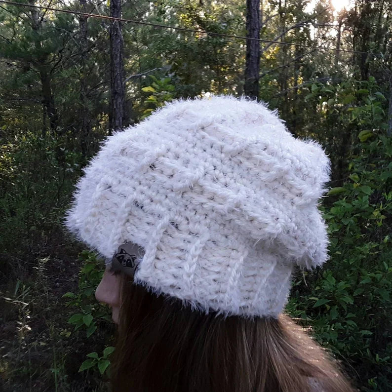Cream crochet winter beanie with ribbed band and textured body, shown from the side on a woman in a forest