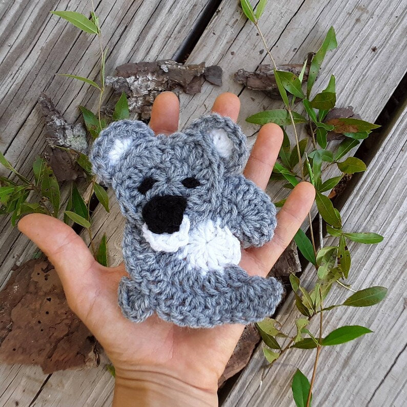 Crocheted koala bear applique in dusty gray with white ears and mouth, black nose and eyes, shown as a finished piece ready to attach to a project