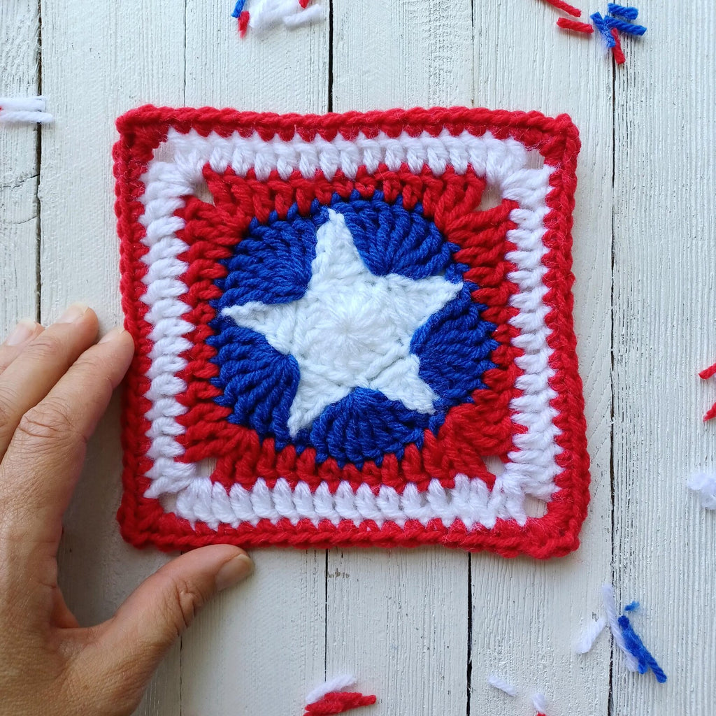 Crocheted red and white granny square with blue star motif, held against white wood