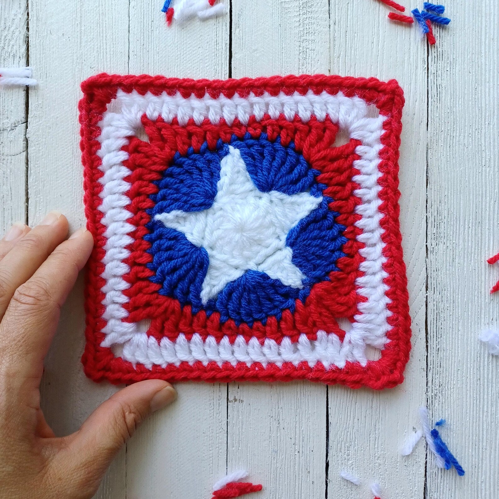 Crocheted red and white granny square with blue star motif, held against white wood