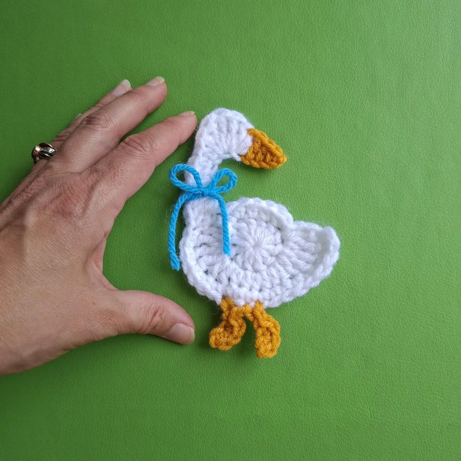 Goose applique crochet piece in white with blue ribbon bow and orange feet held up