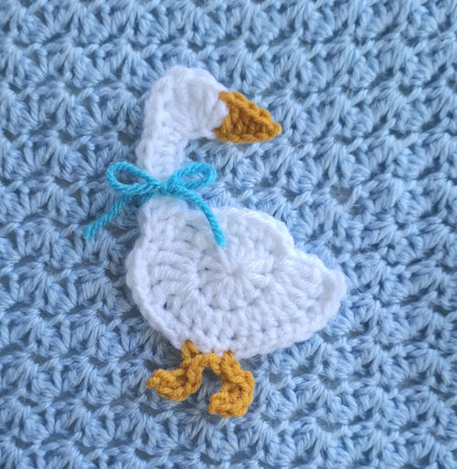 White crocheted goose applique with blue ribbon bow and yellow beak detail
